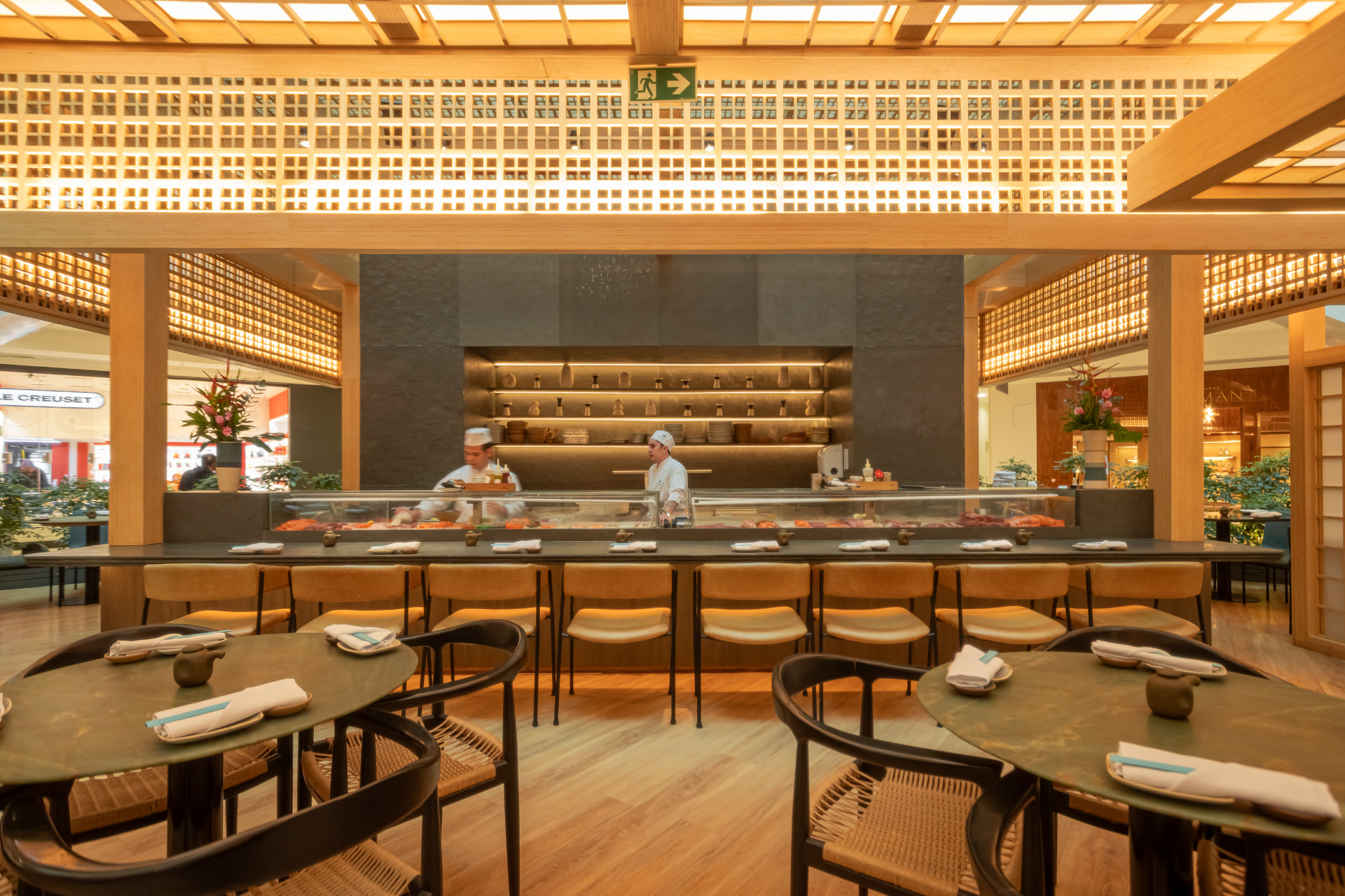 Balcão de sushi do Kitchin Leblon com chefs e iluminação dourada