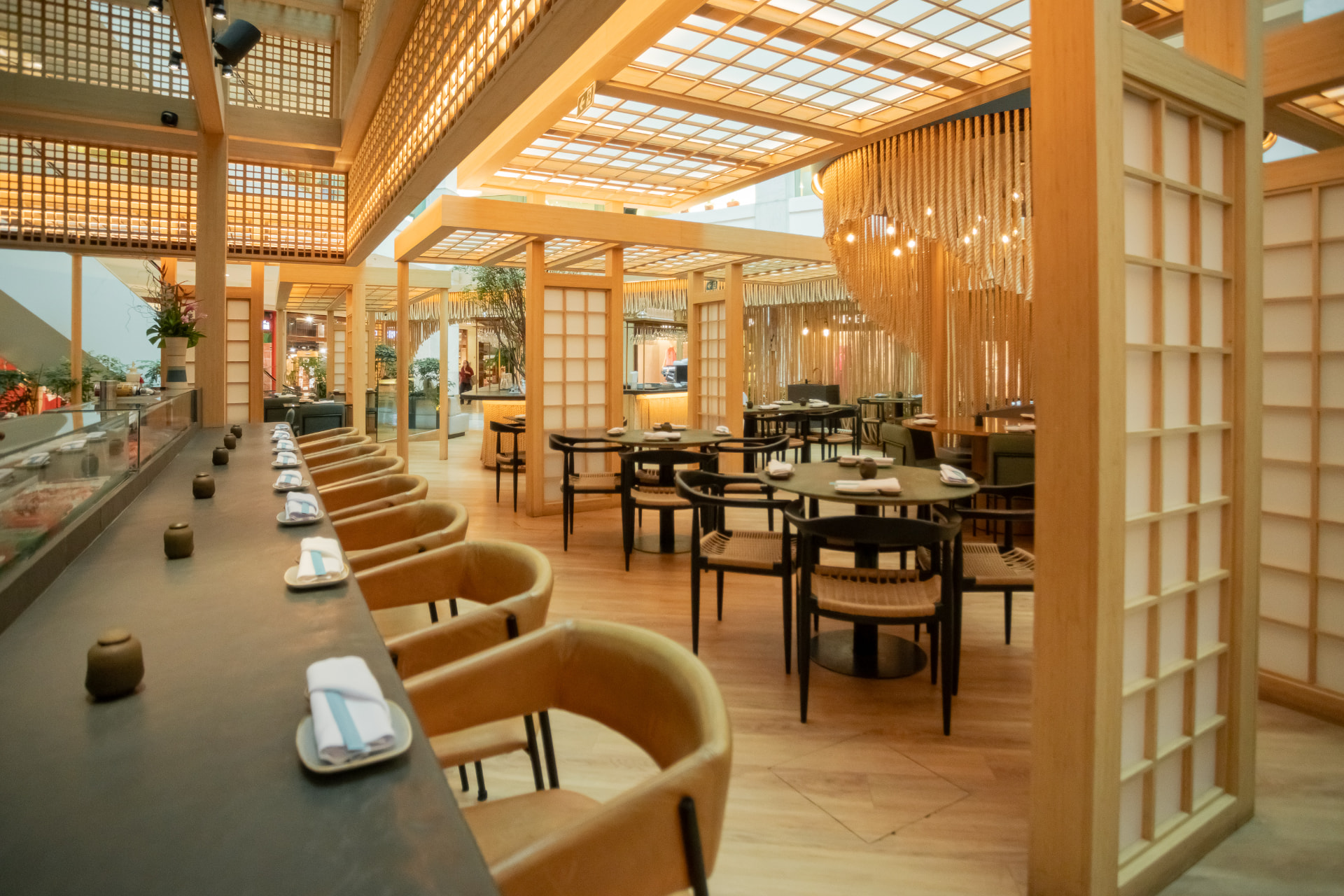 Ambiente do Kitchin Leblon com balcão, mesas e painéis de madeira